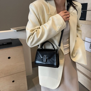 Sac à main Kelly en cuir noir brillant avec boucle argentée porté sur un blazer beige