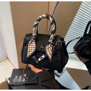 Dettaglio borsa nera in pelle a grana con foulard decorativo in seta sul manico