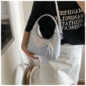Detail of light blue glossy oil wax leather handbag with pearl bow charm worn by model
