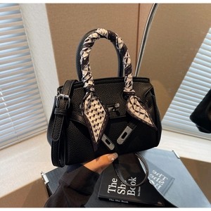 Dettaglio della borsa Kelly in pelle nera con chiusura argento e foulard di seta stampato
