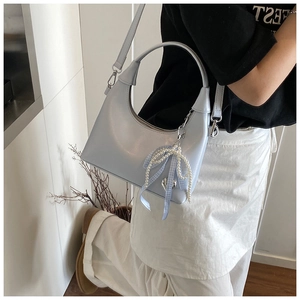 Détail d'un sac à main bleu clair semi-circulaire avec breloque perle et nœud élégant