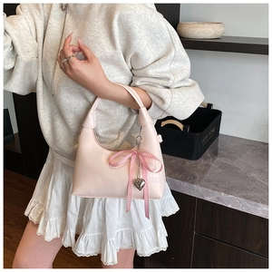 Close-up of pink crescent handbag with plaid bow and silver heart pendant on model