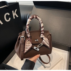 Dettaglio borsa in pelle marrone scuro con manico in seta e chiusura dorata metallica