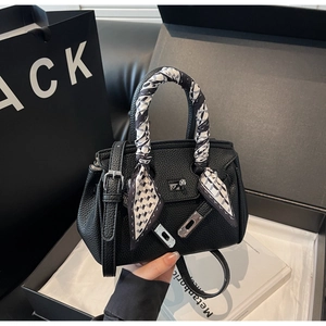 Dettaglio di borsa in pelle nera con chiusura argentata e foulard in seta sul manico