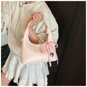 Sac à main en cuir rose avec nœud à carreaux et pendentif cœur tenu par un modèle