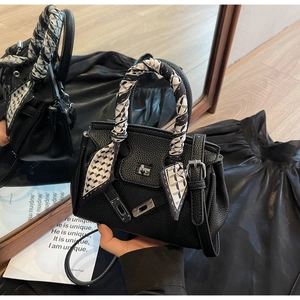 Dettaglio di borsa in pelle nera a grana con chiusura argento e foulard di seta decorativo