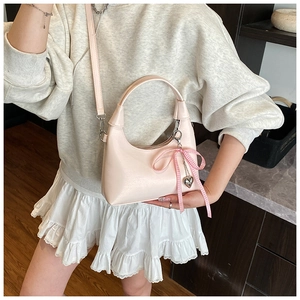 Détail du sac demi-lune rose clair avec un nœud à carreaux et pendentif coeur en métal