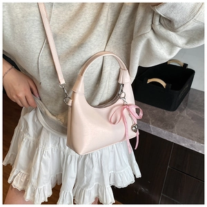 Sac bandoulière demi-lune rose avec nœud, porté par un mannequin dans un décor de style