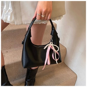 Detail of black faux leather handbag featuring a pearl and pink ribbon bow accessory
