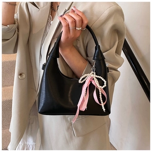 Détail d'un sac à main en cuir noir avec breloque nœud perle et ruban rose élégant