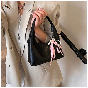 Détail du sac à main noir avec nœud en perles et ruban à carreaux sur un tailleur beige