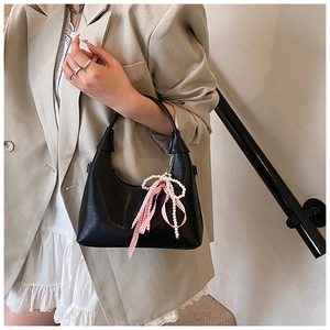Détail d'un sac à main en cuir noir avec un nœud à carreaux rose et des perles
