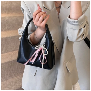 Detail of black semi-circle handbag with pearl bow charm and checkered ribbon