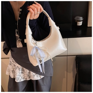 Détail du sac demi-lune en cuir blanc avec nœud bleu, chaîne en perles et pendentif cœur