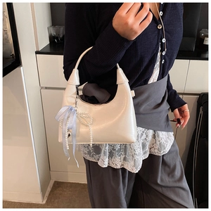 Détail d'un sac demi-lune blanc crème orné d'un pendentif perle avec nœud à carreaux
