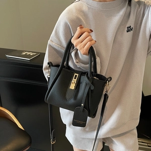 Elegant black lychee leather trapezoid handbag with gold rotating lock and long strap
