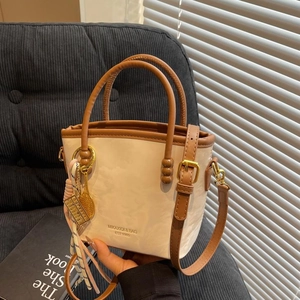 Modische beige Beuteltasche mit braunen Griffen und Tennisanhänger auf grauem Sofa