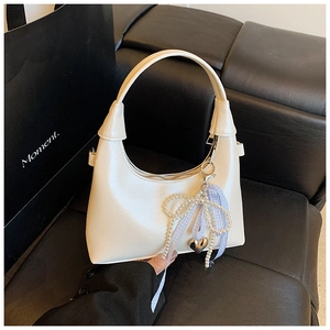 Detail view of cream white half-moon bag with pearl bow charm on a black sofa