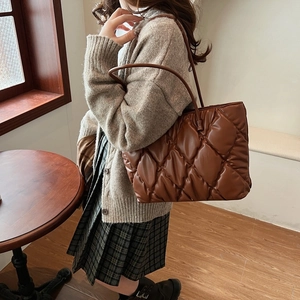 Brown quilted tote bag with diamond stitching shown on shoulder in a cozy indoor setting