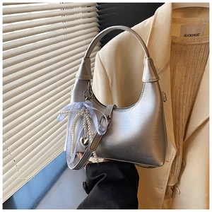 Détail du sac hobo argenté avec un nœud en ruban bleu et un pendentif cœur en perles