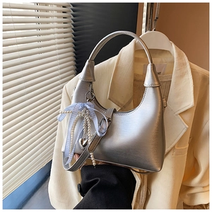 Détail du sac hobo argenté avec texture brossée, pendentif perle et ruban bleu
