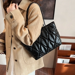 Macro detail of black quilted puffer tote bag with glossy finish and soft padding texture