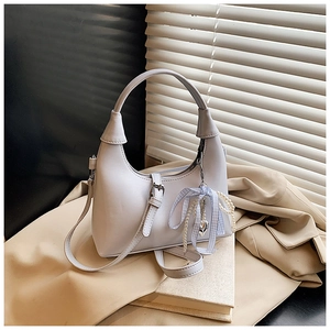 Détail du sac hobo bleu clair avec breloque cœur perle et nœud sur fond de trench-coat