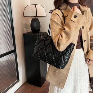 Macro view of black quilted tote bag with soft puffer texture and embroidery details