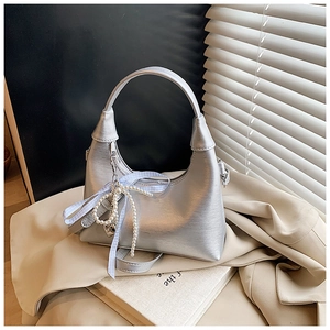 Détail du sac hobo argenté avec breloque perle et ruban sur un blazer beige