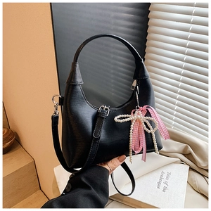 Sac hobo noir tenu à la main avec breloque nœud en perles sur un fond minimaliste