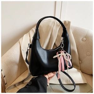 Close-up of black oil wax leather hobo bag with pearl bow charm and pink ribbon detail