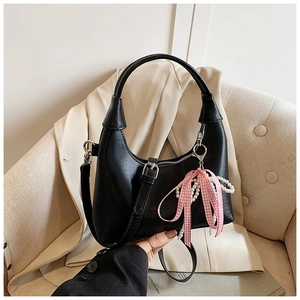 Détail d'un sac à main en cuir noir avec un nœud à carreaux rose et un accessoire en perles