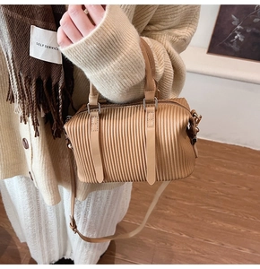 Detail of light brown pleated handbag featuring vertical texture and dual top handles