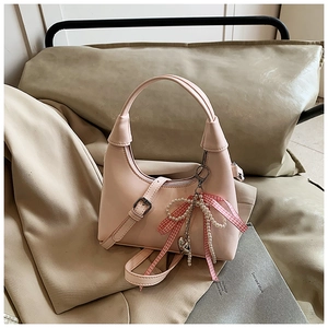Détail du sac à main rose clair avec nœud en tissu, franges perlées et pendentif cœur
