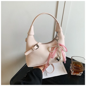 Détail du sac hobo rose clair avec breloques perles et nœud sur table en bois sombre