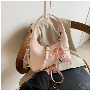 Détail d'un sac demi-lune rose avec nœud perlé et breloque cœur sur siège en bois