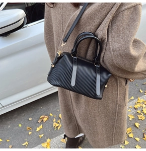 Detailed view of a black pleated Boston bag worn as a crossbody in an autumn street setting