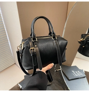Close-up of black pleated texture handbag with gold hardware and cylindrical handle detail