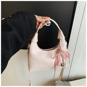 Détail du sac rose en similicuir avec nœud à carreaux, perles et pendentif cœur