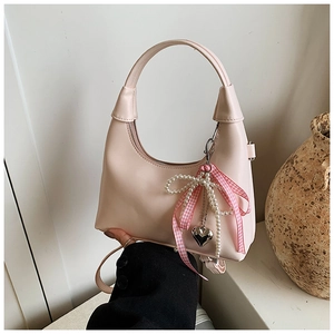 Détail d'un sac à main rose en demi-lune avec nœud perlé et breloque en cœur