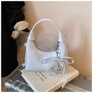 Détail du sac à main demi-lune bleu-argent avec nœud en perles et breloque cœur sur livre