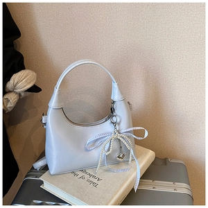 Detail of light blue crescent bag with pearl bow charm on vintage books and luggage