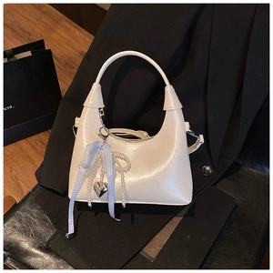 Détail d'un sac blanc brillant avec chaîne de perles, nœud bleu et pendentif cœur sur costume