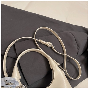 Détail d'un sac bandoulière en similicuir beige avec ruban bleu et breloque perle