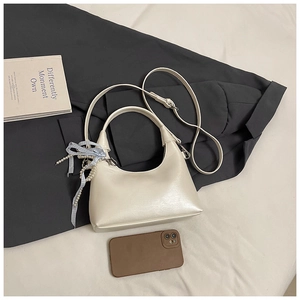 Détail d'un sac à main beige avec un nœud à carreaux bleus et une chaîne de perles