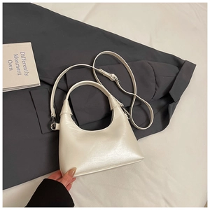 Détail du sac demi-lune blanc au fini nacré posé sur une veste de costume gris foncé