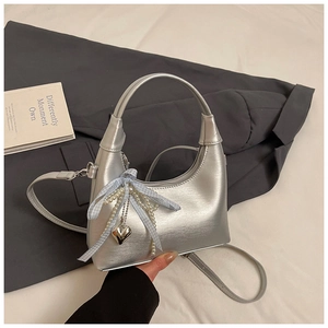 Détail du sac hobo argenté avec nœud bleu, perles et pendentif en forme de cœur