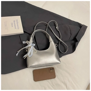 Sac demi-lune argenté avec breloque perle et nœud exposé sur un drap blanc