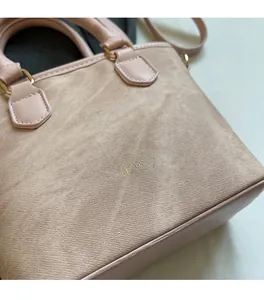 Detail of pink faux suede handbag with golden Fashion & Bags logo and leather handles