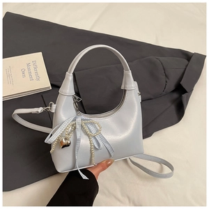 Détail d'un sac à main bleu clair en similicuir avec breloque perle et nœud décoratif